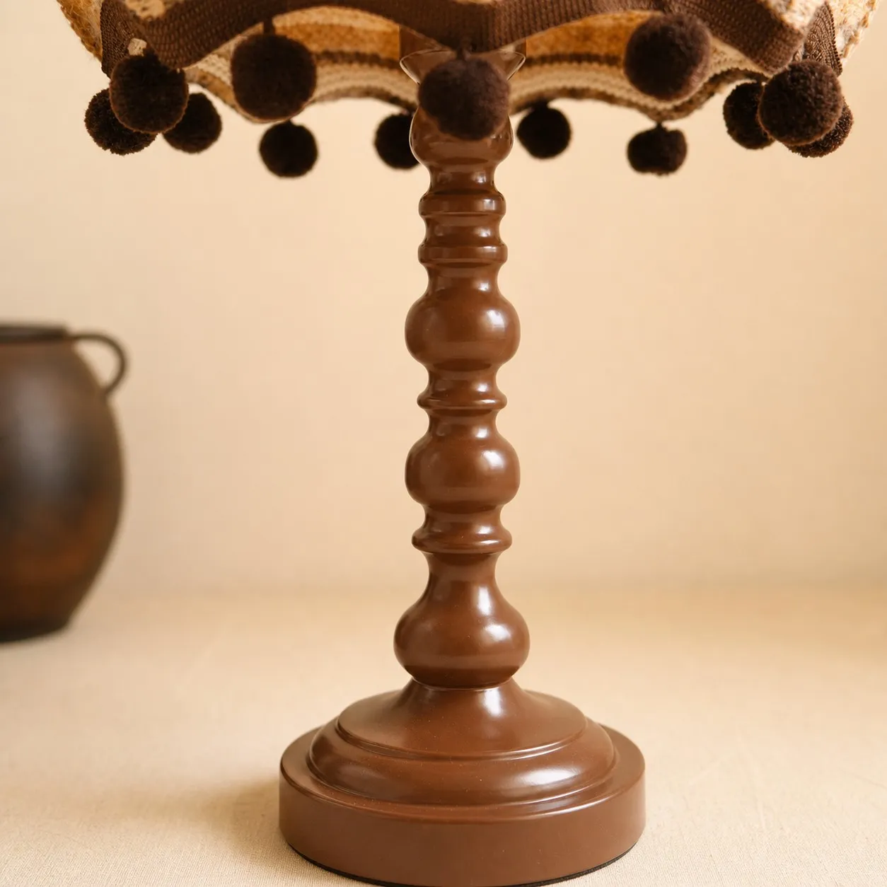 Close view of the turned brown table lamp base and pom pom trim